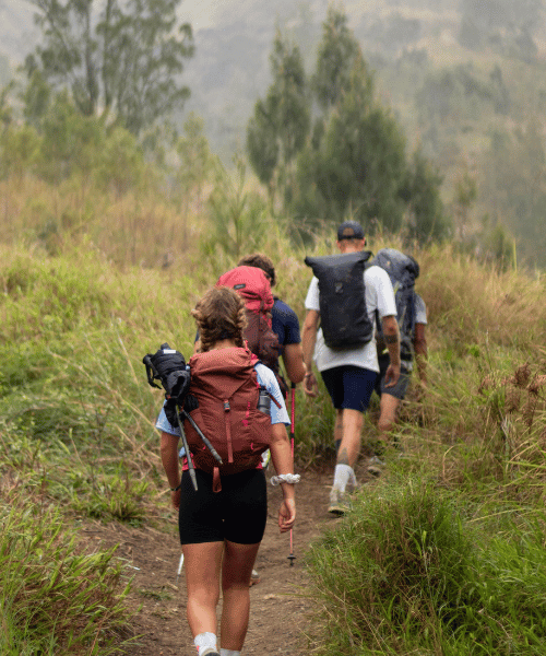 Three hikers climbing a mountain trail in a line, ascending towards the summit with backpacks and hiking gear