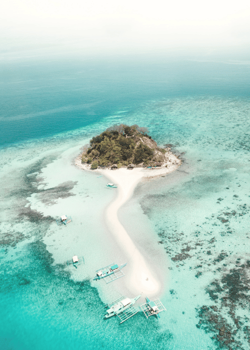 A peaceful island with boats anchored along the shore, surrounded by clear blue water and tropical scenery.