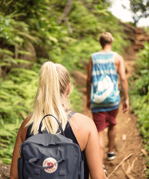 A couple hiking on a mountain trail – the boy is climbing ahead while the girl follows close behind during a scenic outdoor trek.