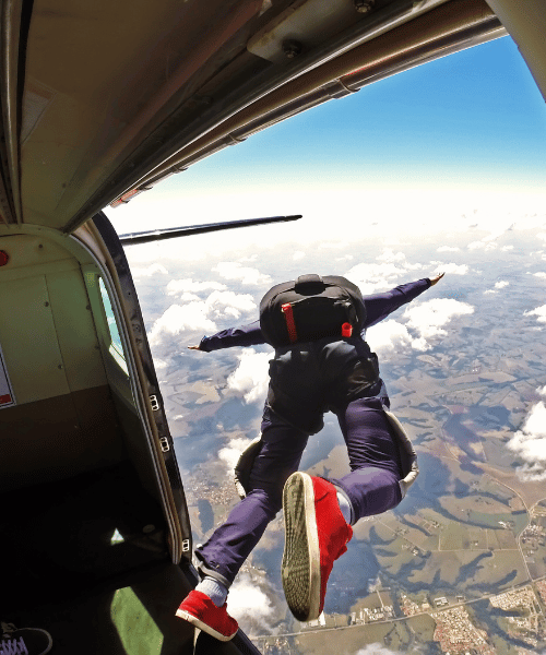 Skydiver preparing to jump – suited up with parachute gear, standing at the edge of the aircraft