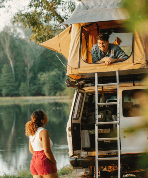 A husband camping on a tree platform while his wife watches from the ground, surrounded by forest during an outdoor adventure.