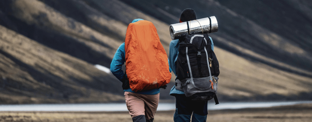 Two hikers climbing a steep mountain along the Laugavegur Trail in Iceland, surrounded by dramatic landscapes and rugged terrain.
