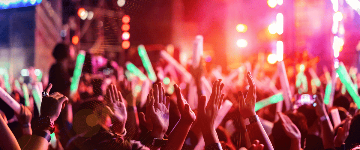 Energetic crowd at a night concert in Georgia with neon glow sticks and vibrant red stage lighting.