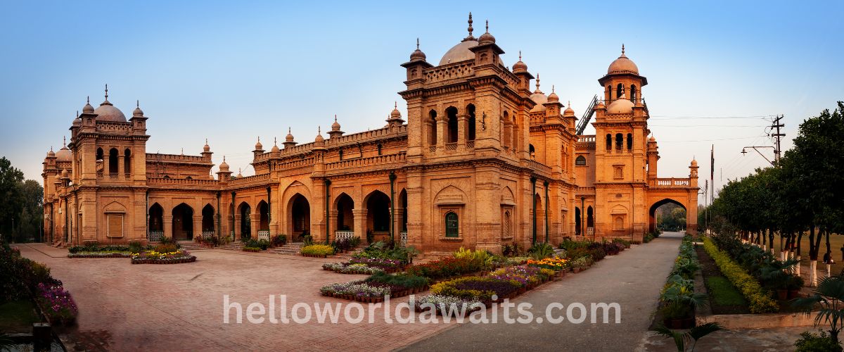 The grand Indo-Saracenic red brick architecture of the University of the Punjab Old Campus in Lahore, featuring ornate domes, arches, and manicured flower beds under a clear blue sky