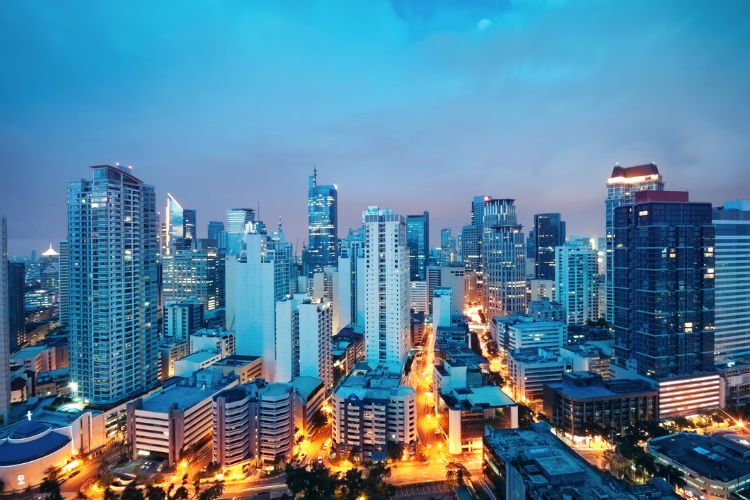 A vibrant aerial night view of the Makati Central Business District skyline in Metro Manila, Philippines, featuring illuminated skyscrapers and city lights.