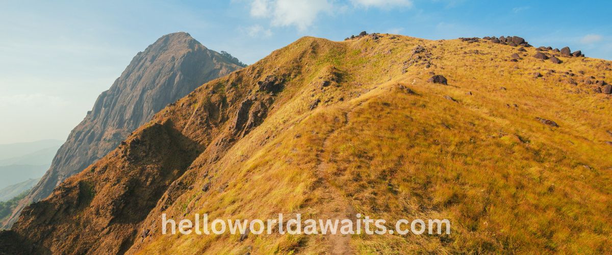 A panoramic view of a rocky island in Myanmar featuring crystal-clear turquoise water, a small white sand beach, and dark jagged rock formations under a bright blue sky.