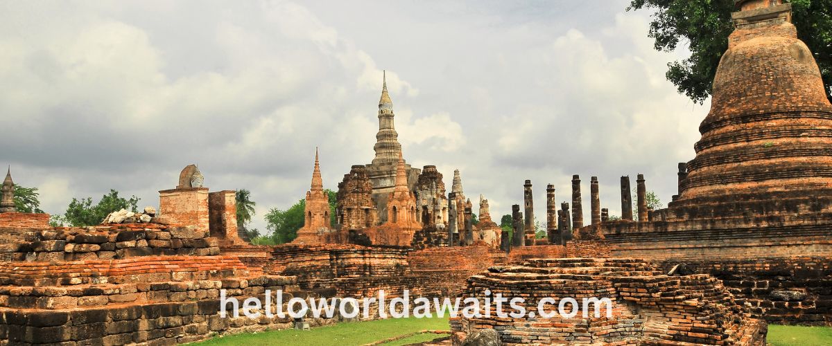 Ancient brick stupas and ruins at the Sukhothai Historical Park under a cloudy sky, a UNESCO World Heritage site in Thailand.