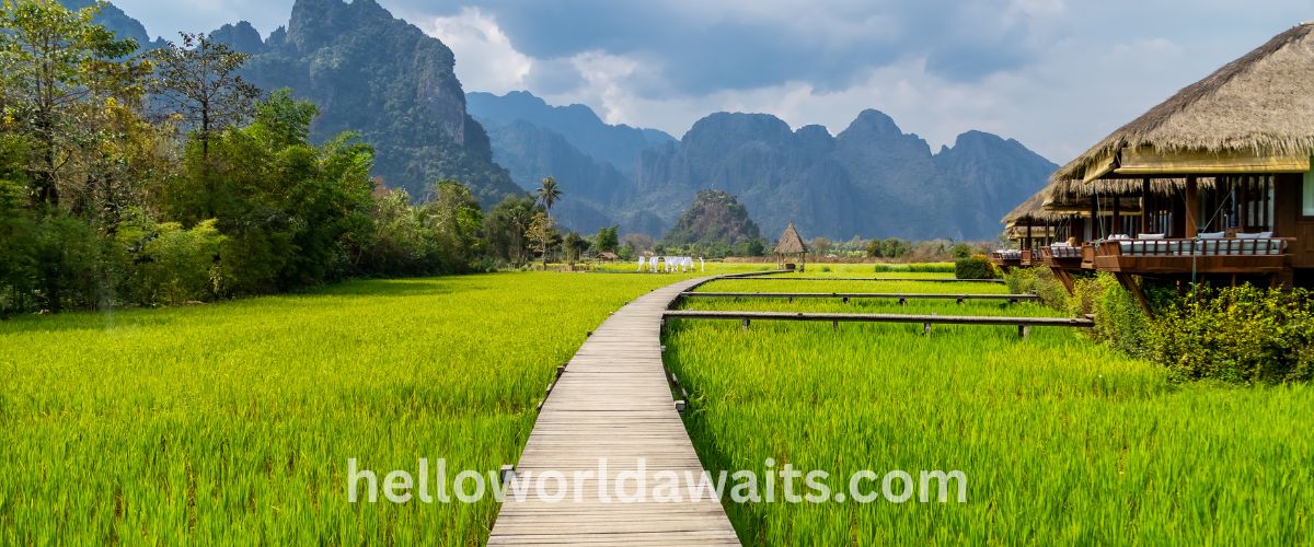 A warm sunset over layered, misty mountain peaks and a river valley, with a bright sun low in an orange sky casting deep shadows over the rugged terrain.