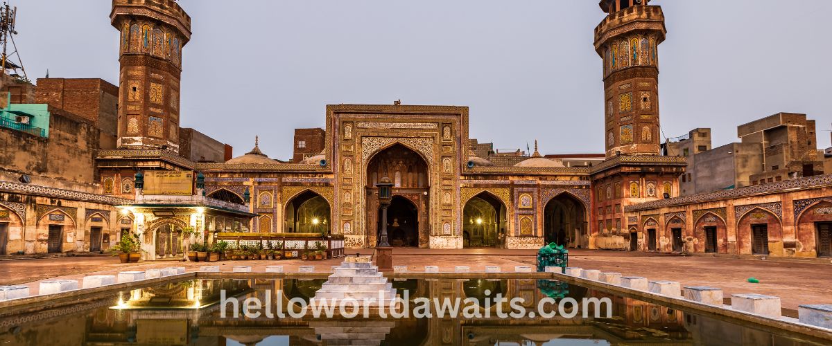 Ornate 17th-century Mughal architecture of Wazir Khan Mosque, showing detailed Kashi-kari tile work and towering minarets reflected in the courtyard water.