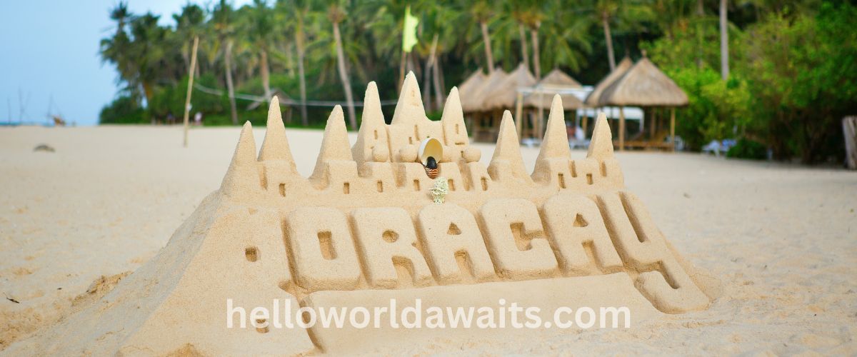A large, detailed sandcastle on the white sand beach of Boracay, Philippines, with the word 'BORACAY' carved into the front. In the background, tropical palm trees and beach huts are visible under a soft daylight