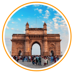 A circular cropped photo of the Gateway of India in Mumbai at dusk. The massive basalt arch is surrounded by tourists, with a bright blue sky and light clouds in the background