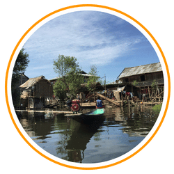 A panoramic view of a rocky island in Myanmar featuring crystal-clear turquoise water, a small white sand beach, and dark jagged rock formations under a bright blue sky.