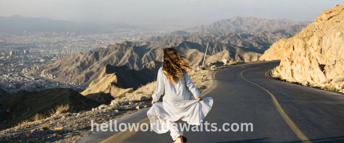 Woman in white dress walking on a winding mountain road overlooking the Kabul city valley, Afghanistan.