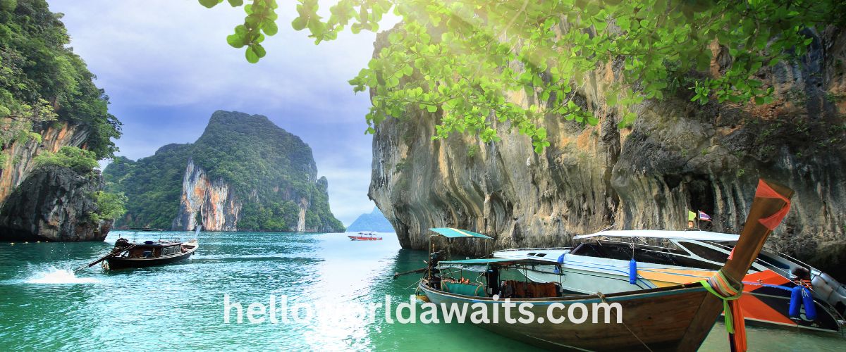 Traditional Thai long-tail boats anchored in turquoise water against massive limestone cliffs and tropical greenery in Thailand.
