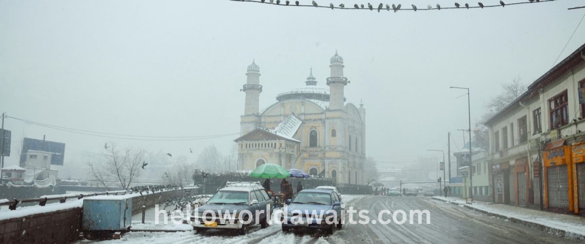 The yellow Shah-Do Shamshira Mosque in Kabul, Afghanistan, during a snowstorm, with cars parked on a slushy road and pigeons perched on overhead wires.